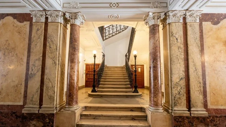 Prunkvoller Eingangsbereich mit Marmorsäulen, Stuckdecken und einer eleganten Treppe, die in die oberen Etagen führt.