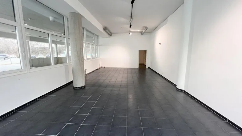 Langer Gewerberaum mit dunklen Fliesen, hohen Decken und sichtbaren Lüftungsrohren an der Decke.