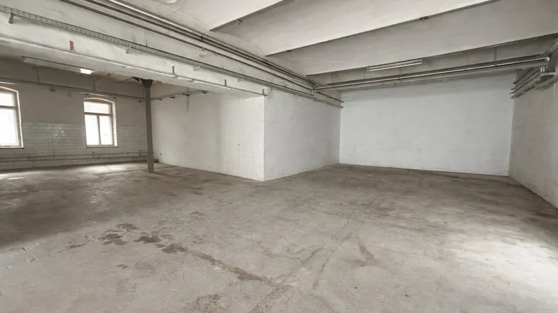 Großer, leerer Raum mit Betonboden, hohen Decken und sichtbaren Leitungen, ideal für gewerbliche Nutzung.