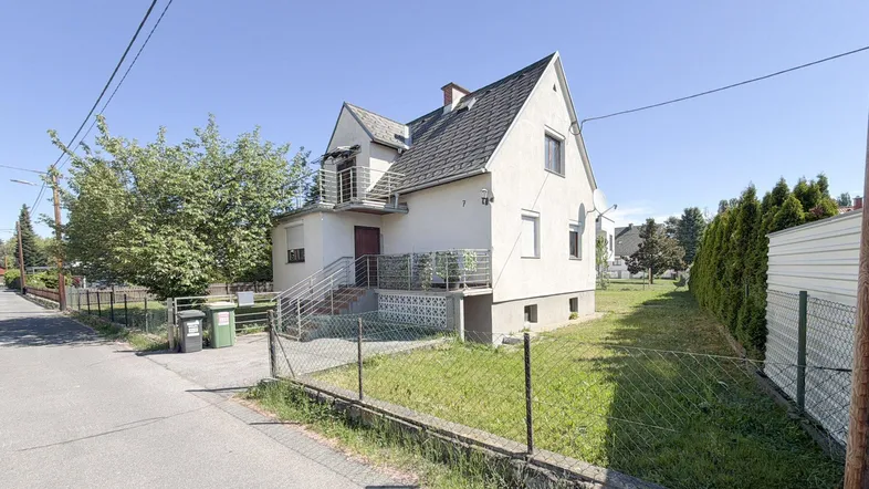 Weißes Einfamilienhaus mit Satteldach, kleinem Balkon und Vorgarten an einem sonnigen Tag.