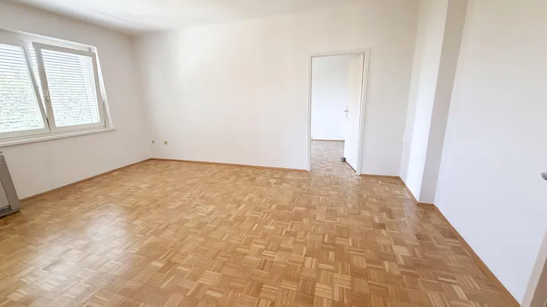 Helles Wohnzimmer mit Parkettboden und Fenster, bereit zur individuellen Gestaltung.