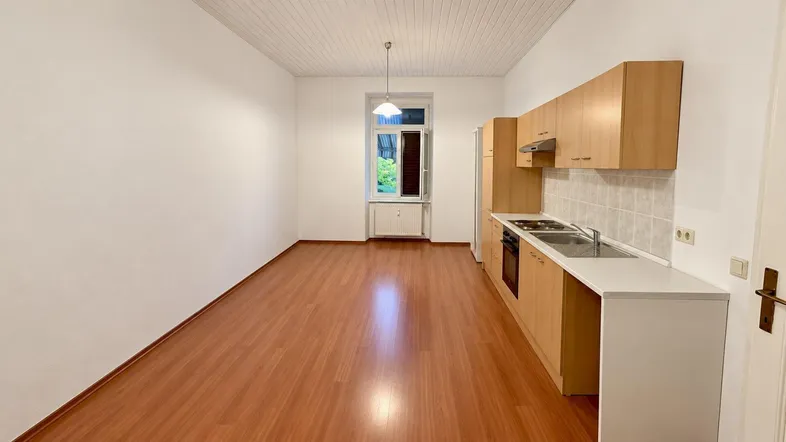 Helle, offene Küche mit Holzschränken, Laminatboden und einem Fenster mit Blick ins Grüne.
