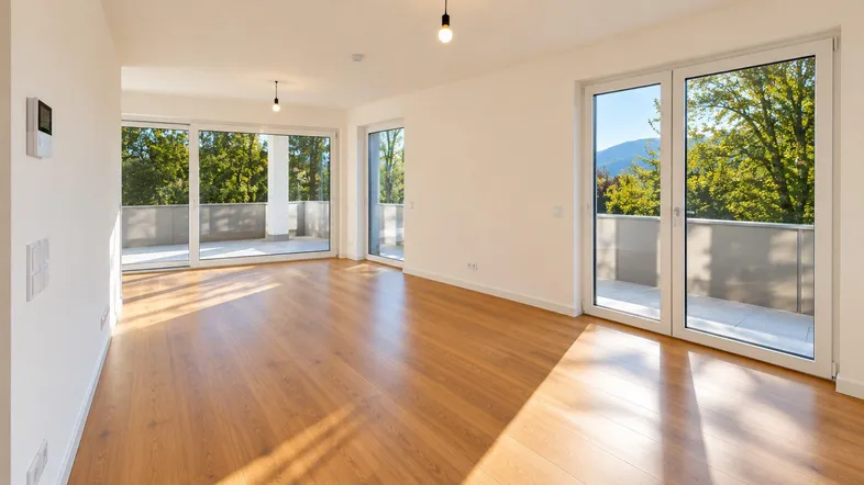 Helles, leeres Wohnzimmer mit Holzboden und Zugang zu einem großen Balkon.