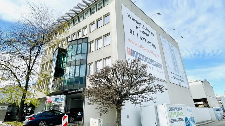 Modernes Bürogebäude mit Glasfassade, Werbeflächen und Zufahrt zur Tiefgarage unter blauem Himmel.
