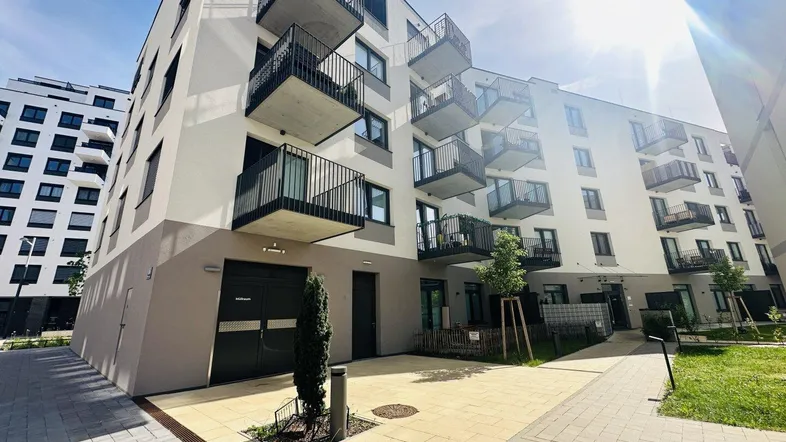 Moderne Wohnanlage mit Balkonen und gepflastertem Vorplatz unter strahlendem Himmel.