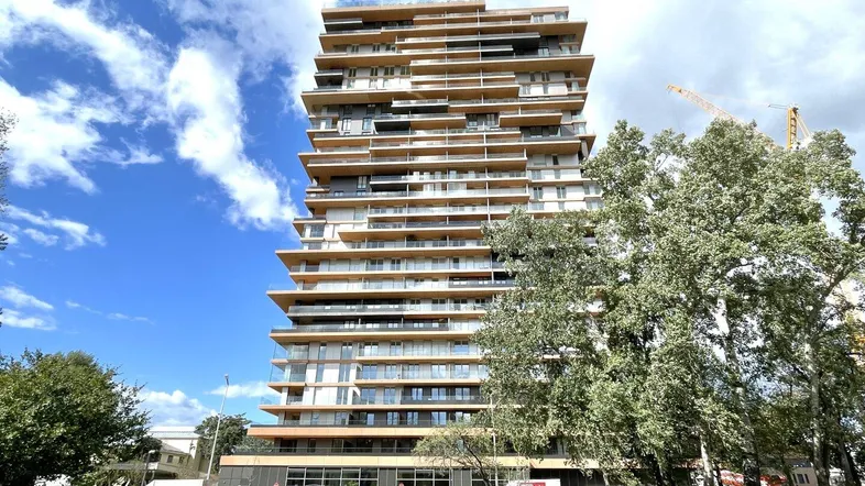 Modernes Hochhaus mit vielen Balkonen und Glasfassade unter blauem Himmel.