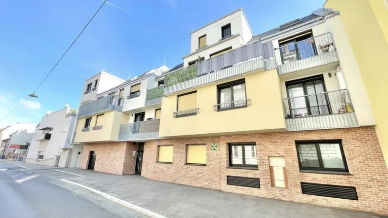 Moderne Wohnhausfassade mit Balkonen und gelben Akzenten unter blauem Himmel.