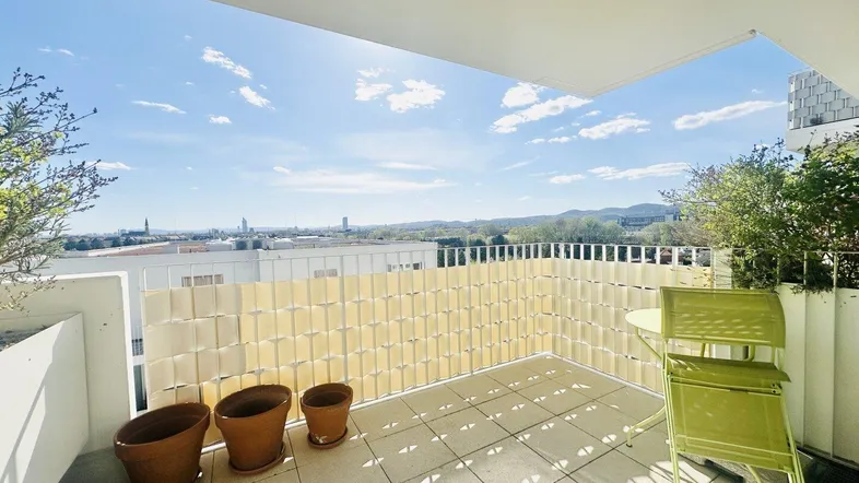 Heller Balkon mit Fliesenboden, einfacher Möblierung und weitem Blick über die Stadt und Landschaft.