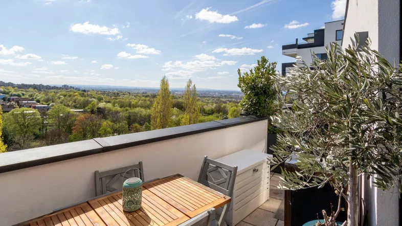 Sonniger Balkon mit Holztisch, Stühlen und weitem Blick ins Grüne.