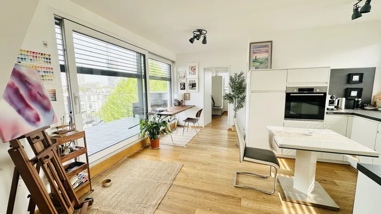 Heller offener Wohn- und Essbereich mit moderner Küche, Holzboden und Zugang zum Balkon.