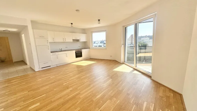 Heller offener Wohnbereich mit integrierter Küche, Parkettboden und Zugang zu einem Balkon.
