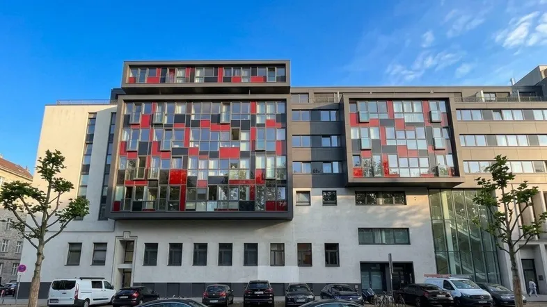 Moderne Gebäudefassade mit markanten roten und grauen Paneelen sowie großen Fenstern.