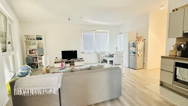 Heller offener Wohn- und Essbereich mit modernem Sofa, Holzboden und integrierter Küche.