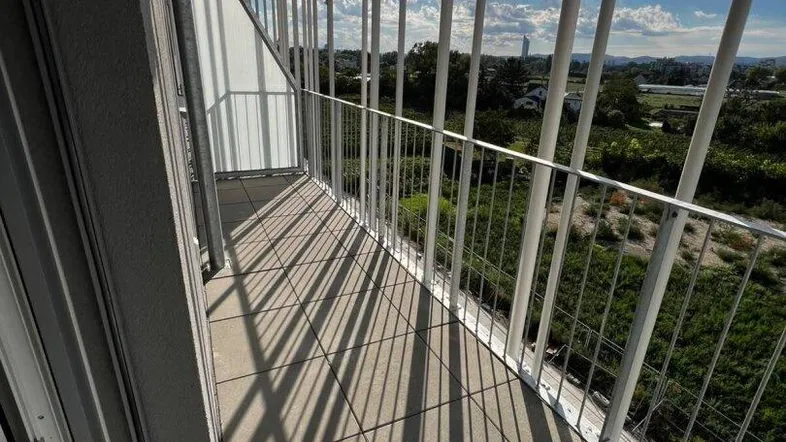 Heller Balkon mit moderner Metallbrüstung und weitem Blick über grüne Landschaft unter blauem Himmel.