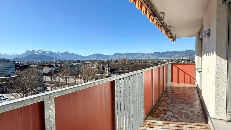 Heller Balkon mit Markise, Fliesenboden und weitem Blick auf die Berge und die Stadt.