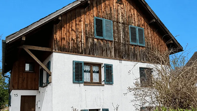 Traditionelles Haus mit Holzfassade und grünen Fensterläden unter blauem Himmel.