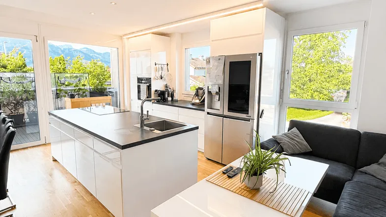 Heller offener Wohn- und Essbereich mit moderner Küche, Holzboden und Zugang zum Balkon mit Bergblick.