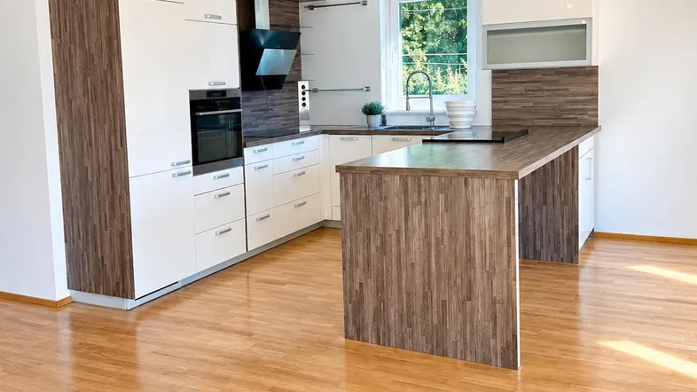 Moderne Küche mit weißen Schränken, Holzdekor, Kücheninsel und Blick ins Grüne.