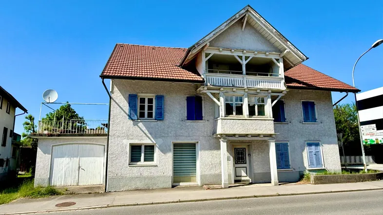 Vorderansicht eines gepflegten Altbaus mit blauen Fensterläden und einem Balkon im Obergeschoss.