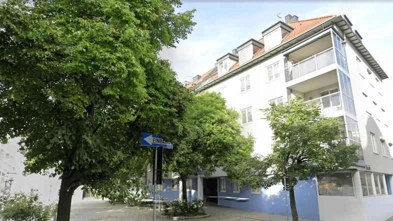 Mehrfamilienhaus mit weißer Fassade, Balkonen und einem externen Aufzug in städtischer Umgebung.