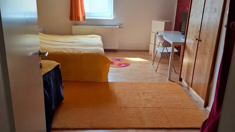 Helles Schlafzimmer mit Holzboden, einem Bett, Schreibtisch und Kleiderschrank.