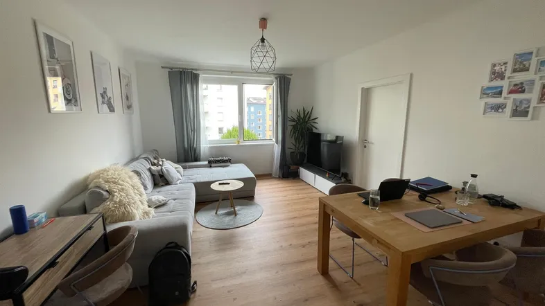 Heller Wohn- und Essbereich mit modernem Sofa, Holzboden und Blick ins Grüne.