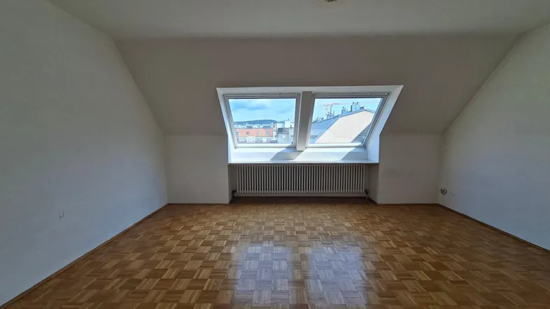 Helles Zimmer im Dachgeschoss mit Parkettboden und Dachfenstern, ideal als Schlafzimmer nutzbar.
