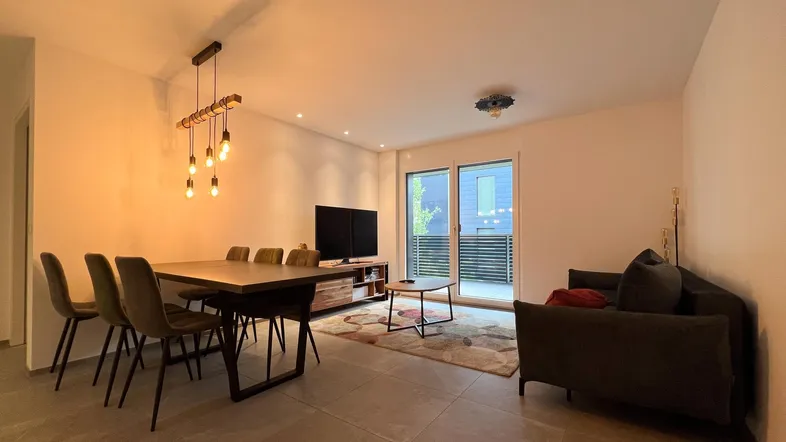Moderner offener Wohn- und Essbereich mit Fliesenboden und Zugang zum Balkon.