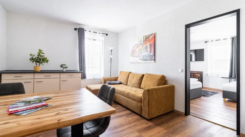 Helles Wohn- und Esszimmer mit Holzboden, bequemer Couch und Blick in ein weiteres Zimmer.