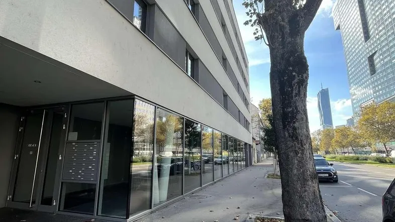 Moderne Gebäudefassade mit großen Glasflächen im Erdgeschoss und städtischer Umgebung.
