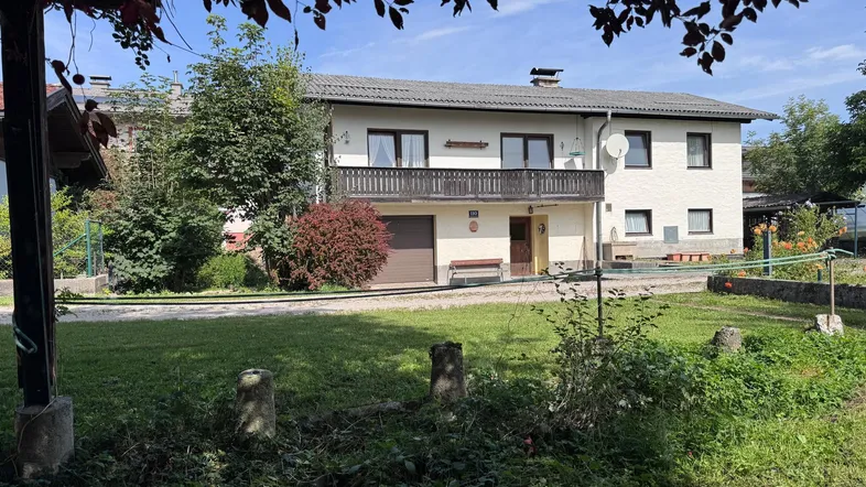 Zweistöckiges Wohnhaus mit Balkon und integrierter Garage, umgeben von einem grünen Gartenbereich.