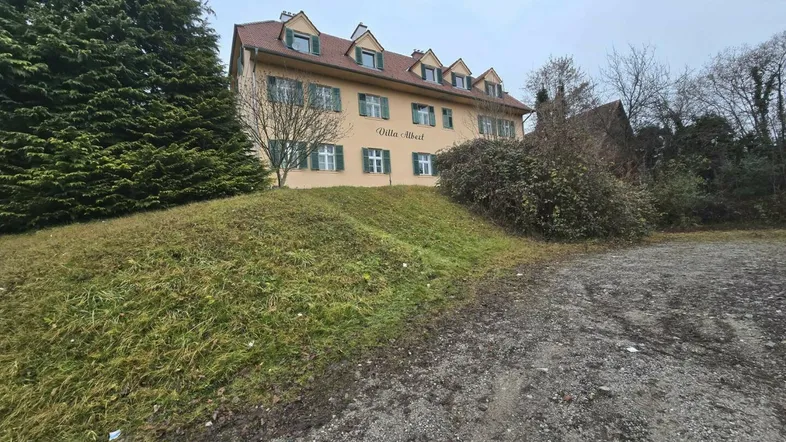Historische Villa mit gelber Fassade, grünen Fensterläden und umgebender Natur auf einem Hügel.