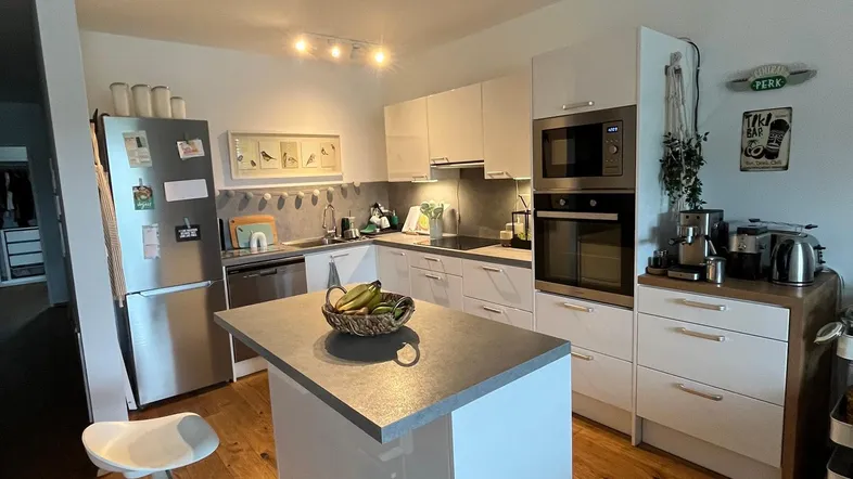 Moderne offene Küche mit Kochinsel, weißen Hochglanzfronten, Holzboden und integrierten Geräten.