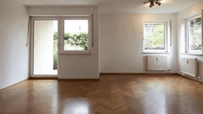 Helles Wohnzimmer mit Fischgrätparkettboden, großen Fenstern und Zugang zum Balkon.
