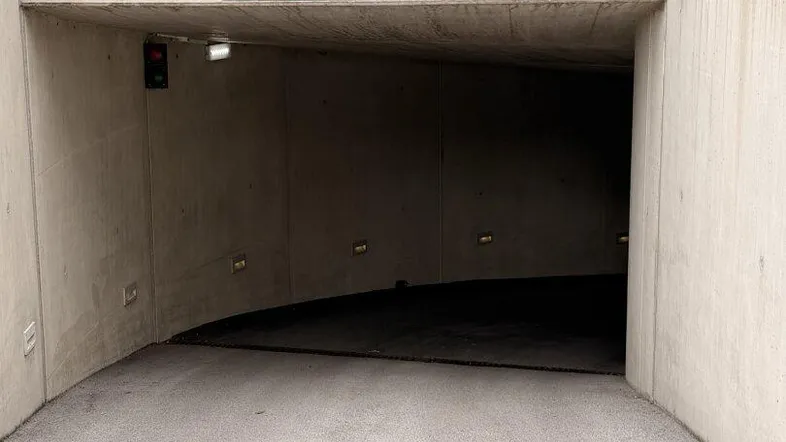 Einfahrt zu einer Tiefgarage mit Betonwänden, einer Rampe und Hinweisschildern für die Nutzung.