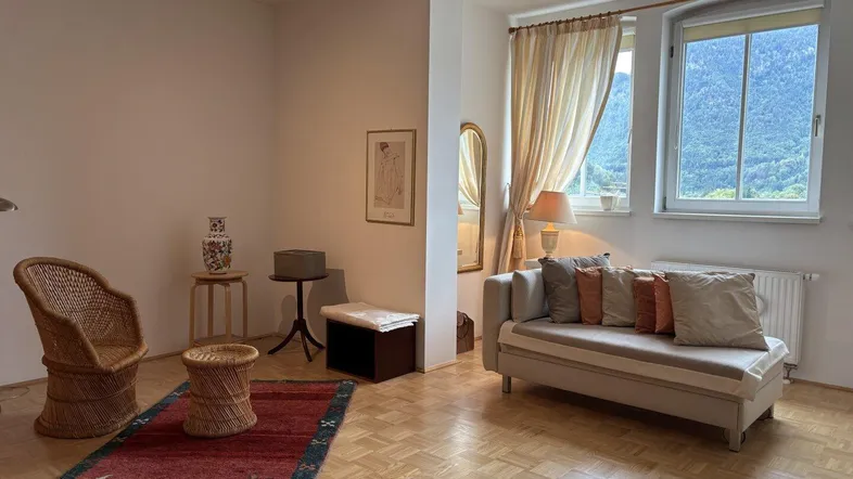 Helles Wohnzimmer mit Parkettboden, bequemer Chaiselongue und Blick auf die umliegende Berglandschaft.