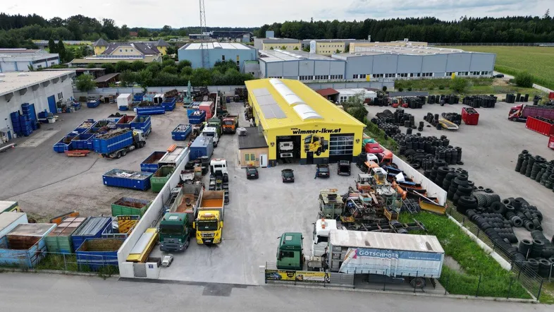 Luftaufnahme eines Gewerbegebiets mit einer großen gelben Halle, umgeben von Lagerflächen und Feldern.
