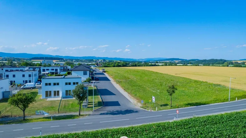 Luftaufnahme einer neuen Wohnsiedlung umgeben von grünen Feldern unter blauem Himmel.