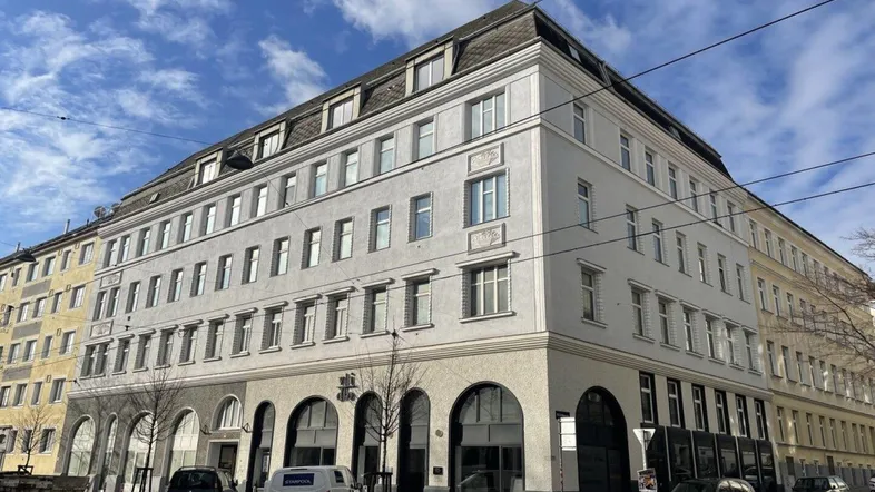 Mehrstöckiges Wohngebäude mit klassischer Fassade und Mansarddach in städtischer Umgebung.