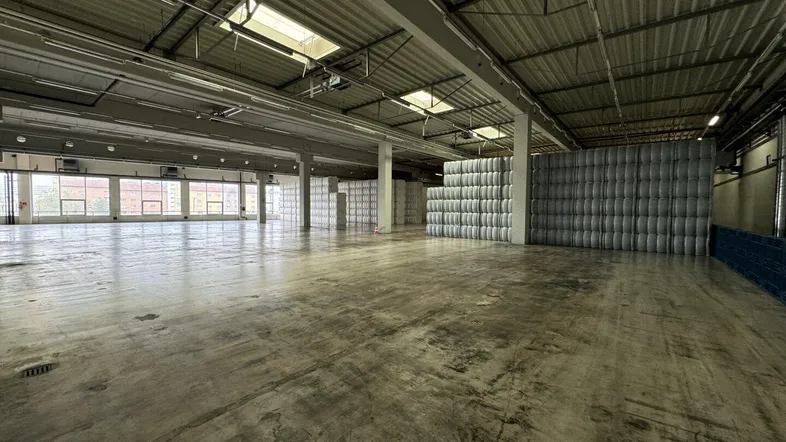 Große, offene Lagerhalle mit Betonboden, hohen Decken und Oberlichtern, ideal für industrielle Nutzung.