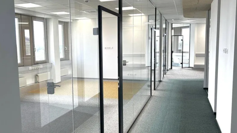 Langer Bürogang mit modernen Glaswänden, der zu mehreren hellen Büroräumen führt.