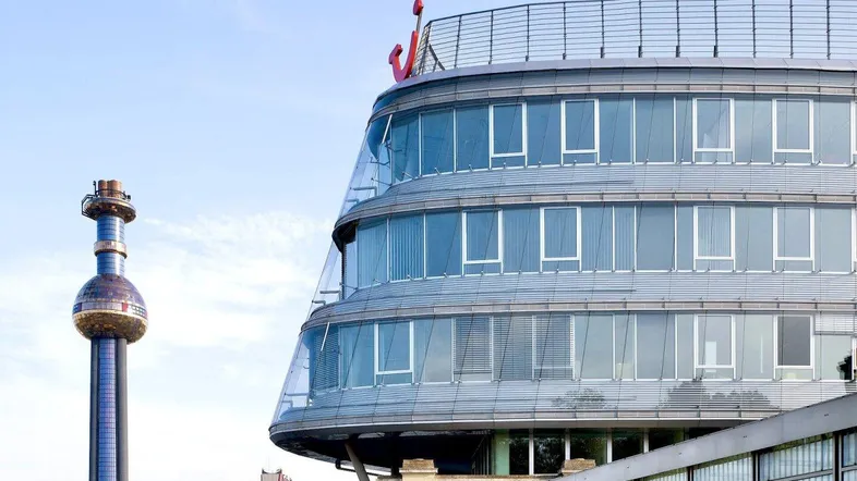 Modernes Bürogebäude mit geschwungener Glasfassade und einem Turm im Hintergrund unter blauem Himmel.