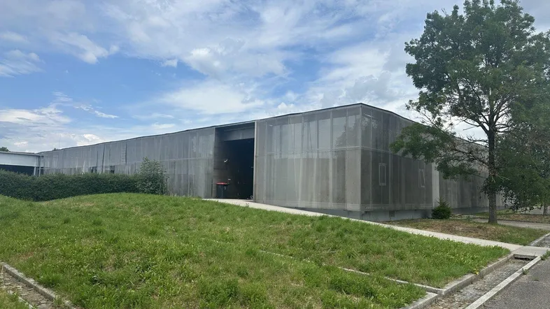 Moderne Gewerbeimmobilie mit langer Metallfassade und Grünflächen unter bewölktem Himmel.