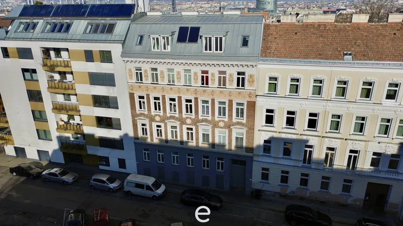 Luftaufnahme der Gebäudefassade mit verschiedenen Baustilen und Solarpaneelen auf dem Dach.