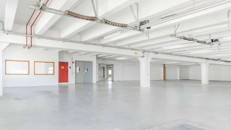 Großer, leerer Lagerraum mit hohen Decken, Betonboden und sichtbaren Installationen an der Decke.