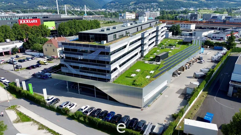 Luftaufnahme eines modernen Bürogebäudes mit begrüntem Dach, Solaranlagen und umliegenden Parkplätzen in städtischer Umgebung.