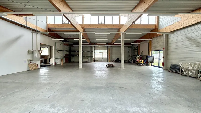Geräumige Lagerhalle mit hohen Decken, Holzbalken und Betonboden, ideal für gewerbliche Nutzung.