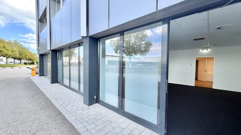 Moderne Geschäftsfassade mit großen Glasfronten und Zugang zu einem leeren Gewerberaum.