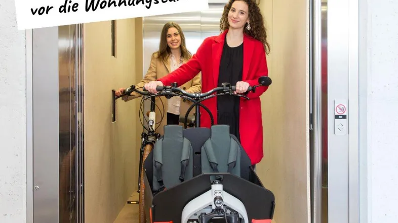 Zwei Frauen mit einem Lastenrad in einem modernen Aufzug, der den Transport bis zur Wohnungstür ermöglicht.