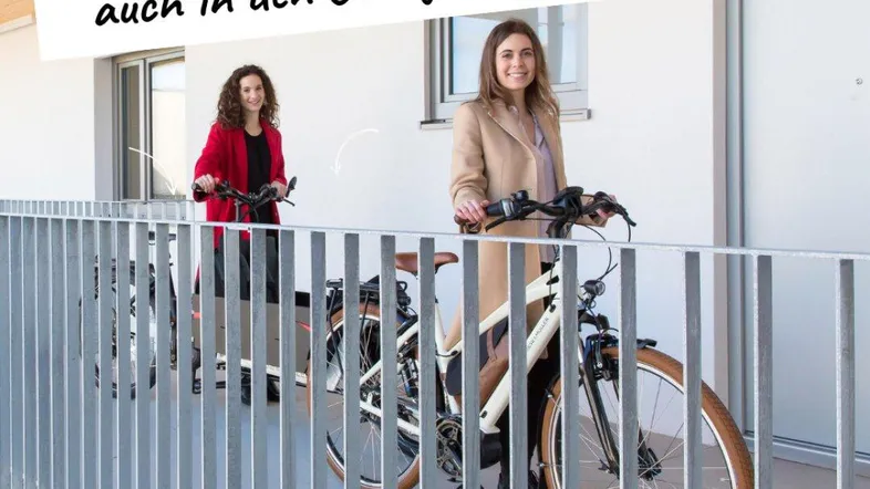Frauen mit Fahrrädern auf einem hellen Laubengang, der direkten Zugang zu den Wohnungen bietet.